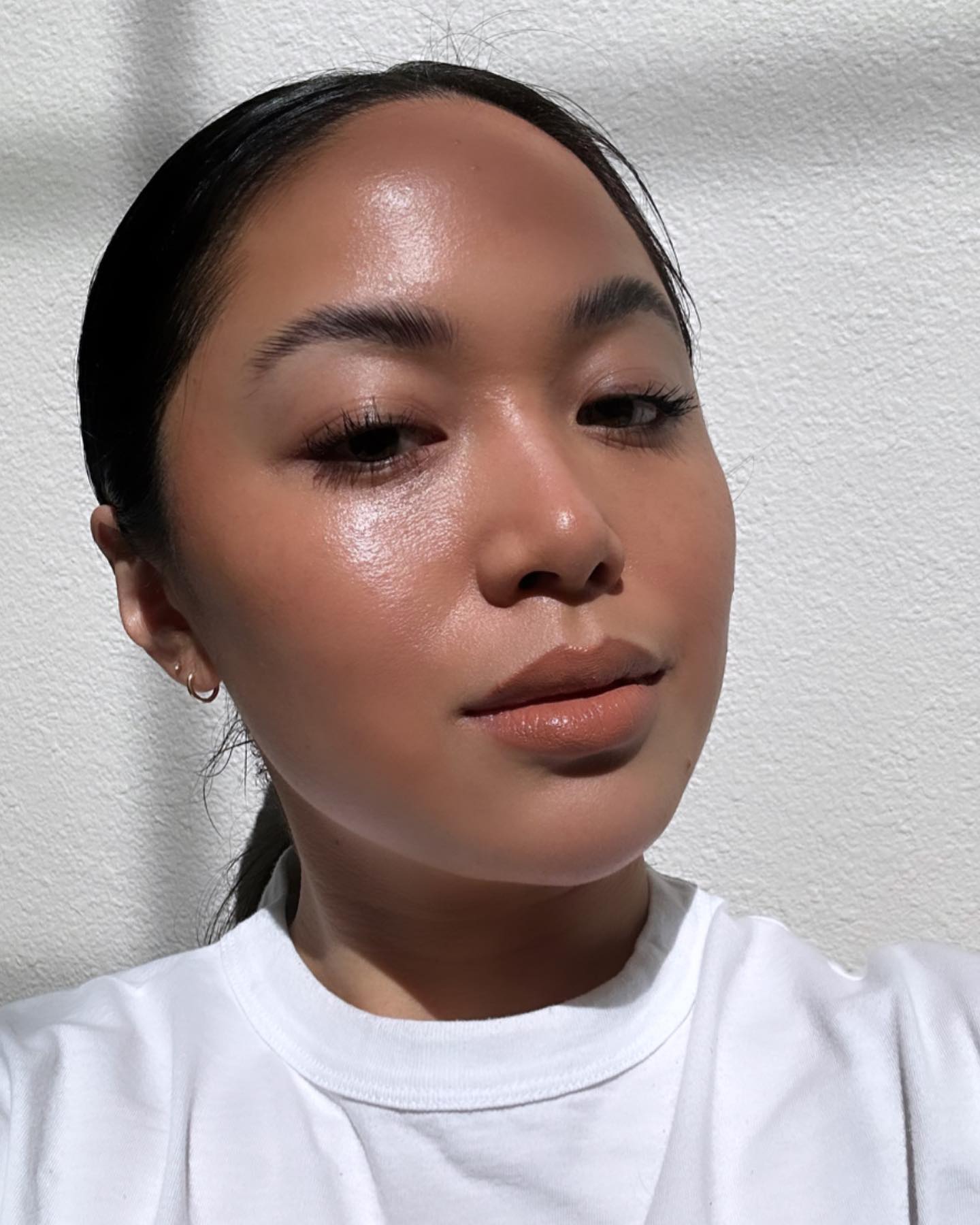 一位身穿白色 T 卹、皮膚發光的女子自拍的照片