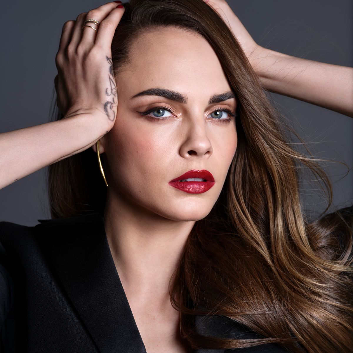 卡拉迪樂芬妮 (Cara Delevingne) 在灰色背景下塗著紅色口紅、畫著帶翅膀的眼線的照片。