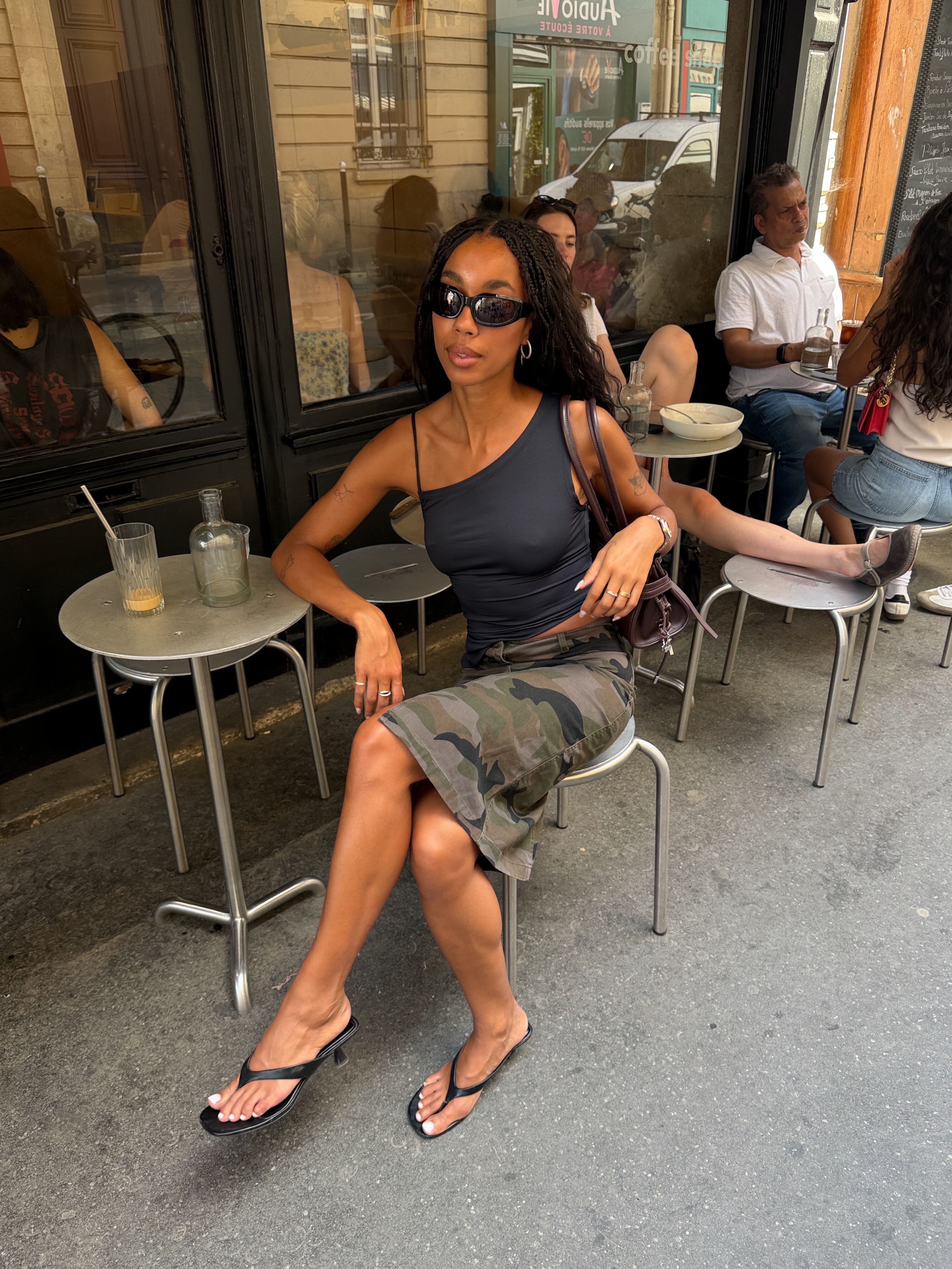 @amaka.hamelijnck 穿著長工裝短褲、高跟人字拖和不對稱上衣的圖片。