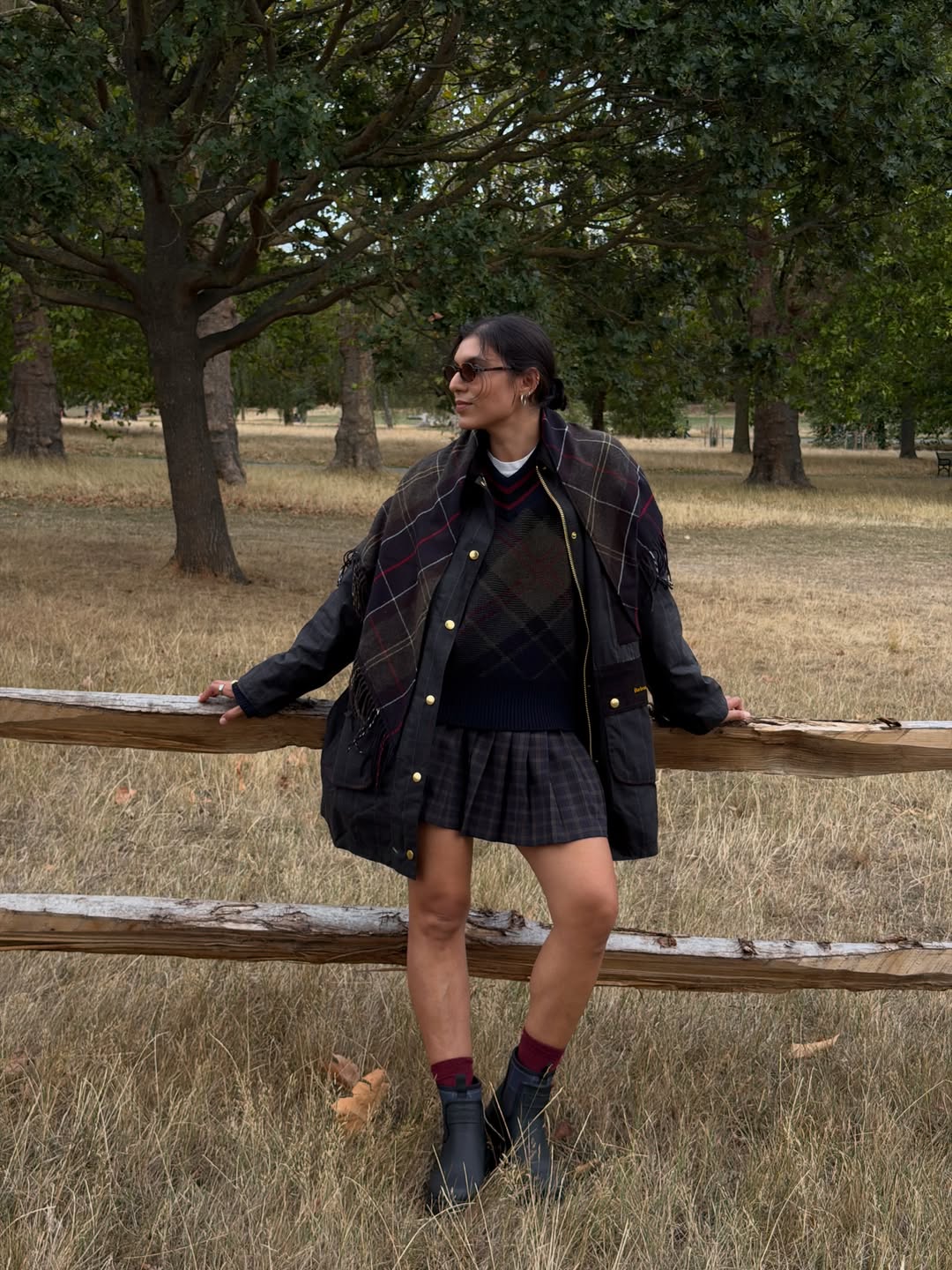 印度卡多納 (India Cardona) 斜倚在木柵欄上，穿著海軍藍格紋夾克和褶皺迷你裙